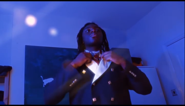 Joven ajustándose la chaqueta en una habitación con iluminación azul y fondo de pizarra.