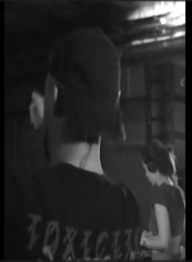 Dos personas, una con sombrero y otra con gafas, en un ambiente oscuro, posiblemente en un espacio cerrado.