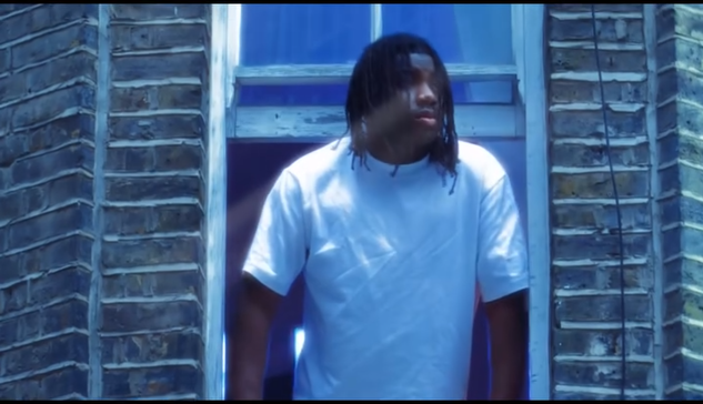 Un joven con camiseta blanca asomándose por una ventana con paredes de ladrillo.