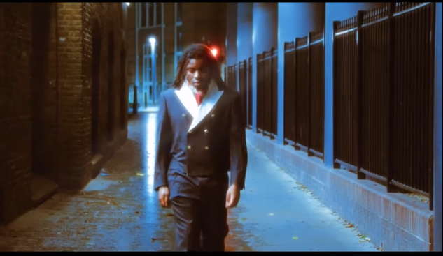 Mujer caminando por una calle iluminada en la noche, vestida con un traje formal oscuro