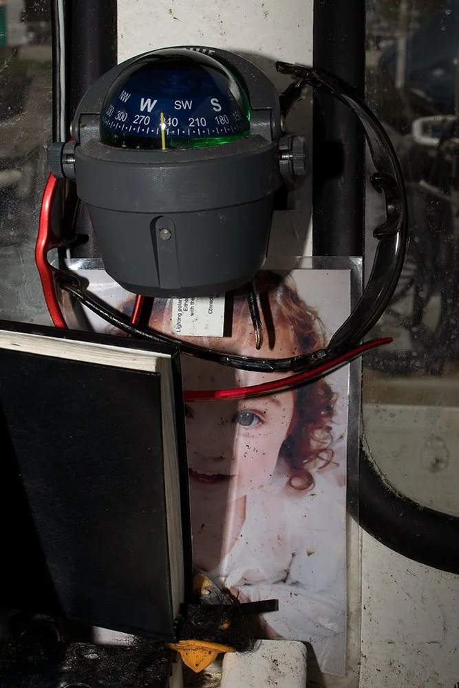 A close-up of a compass mounted on a glass surface, with wires and a photo of a girl with curly red hair and a white shirt beneath it.