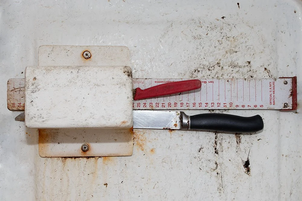 A meat slicer with a red handle and a black handle, placed on a white surface.