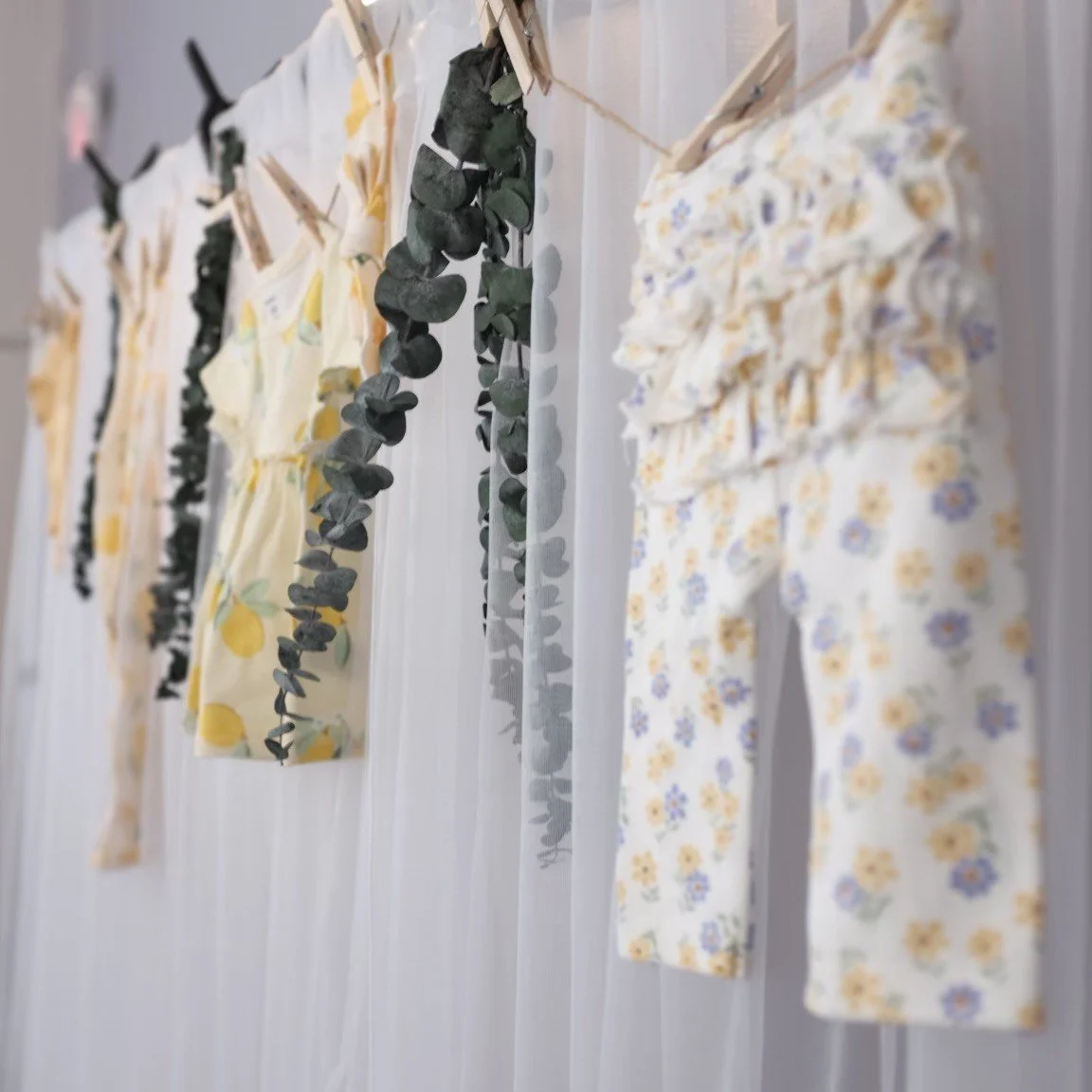 Rows of children's clothing hanging on a line with clothespins, decorated with green leaves and floral patterns.