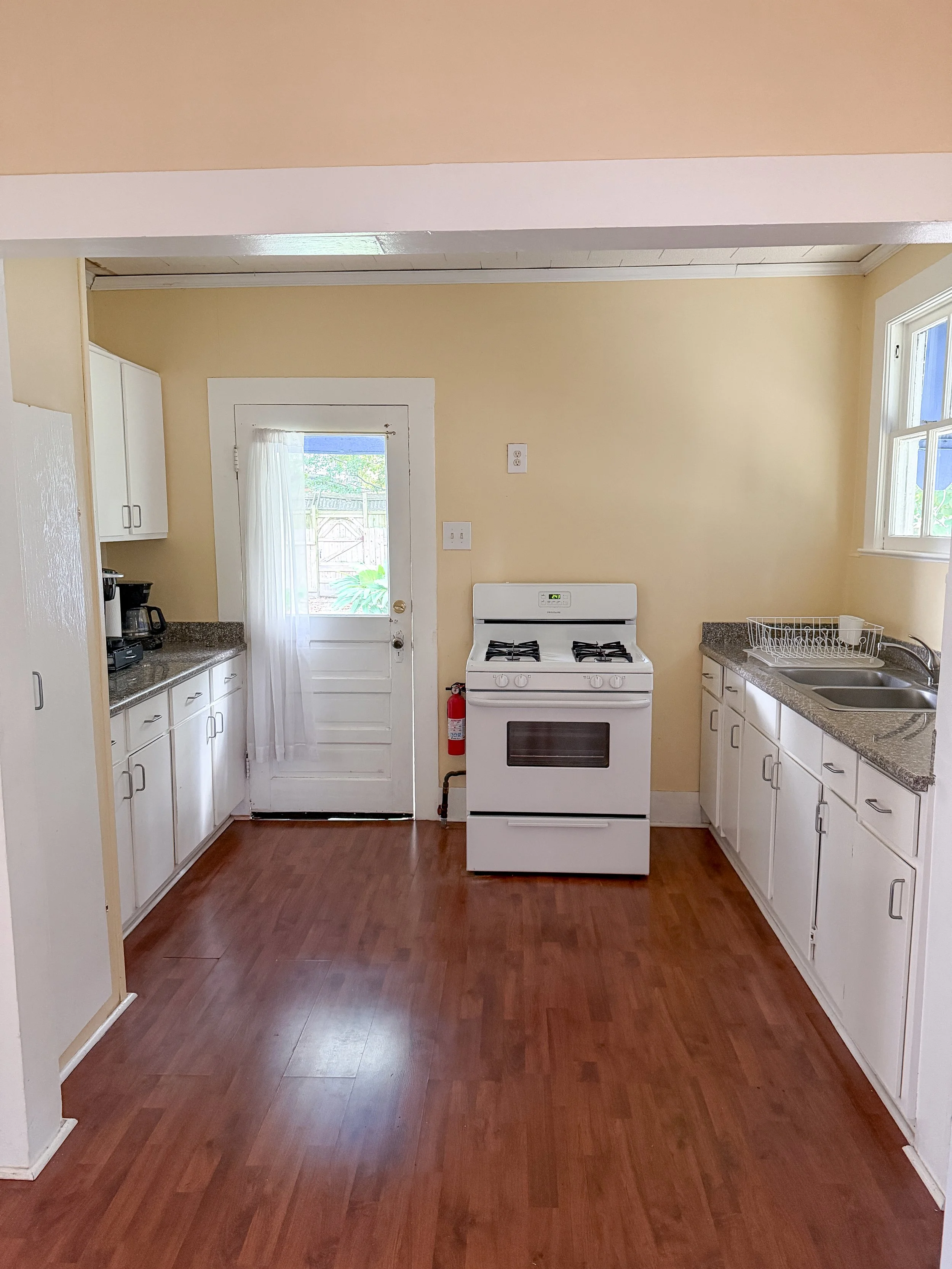 Kitchen with white cabinets, a white stove, a double sink, a window, and a door leading outside.