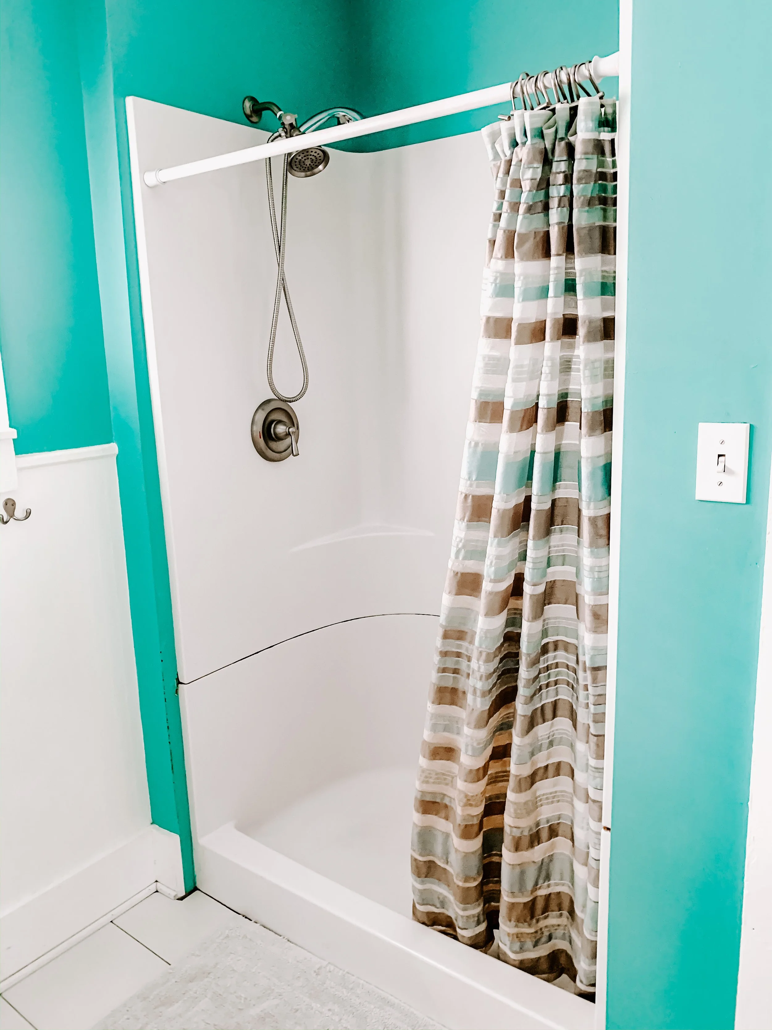 Small bathroom shower with a striped curtain, teal walls, white shower walls, and a handheld showerhead.