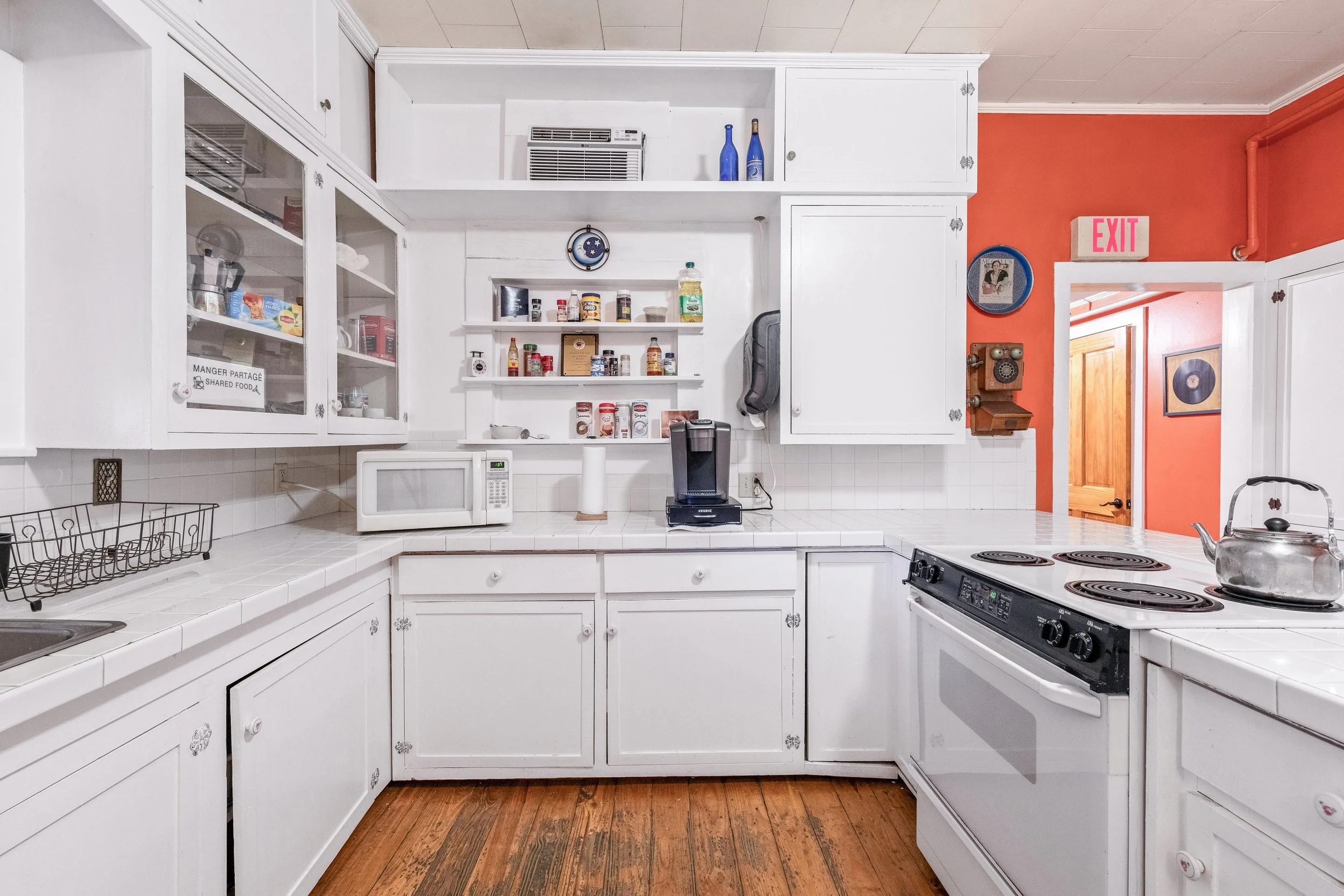 Kitchen with white cabinets, stove, microwave, and coffee maker, red wall, and hallway with wooden door