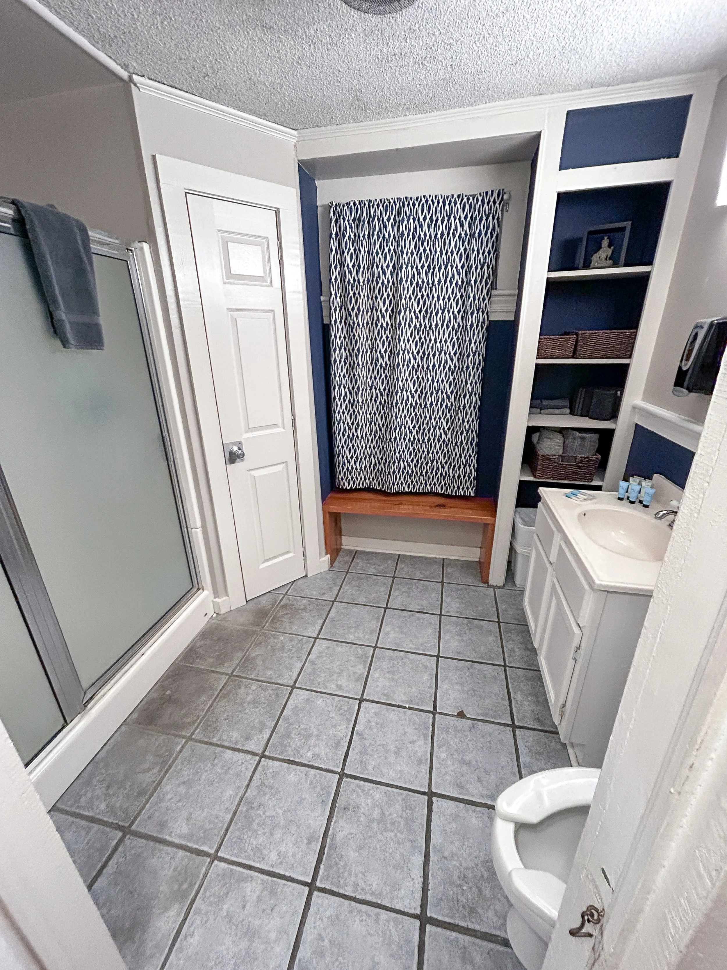 Bathroom with a shower, a white storage cabinet, a small sink, and a stool with a curtain.