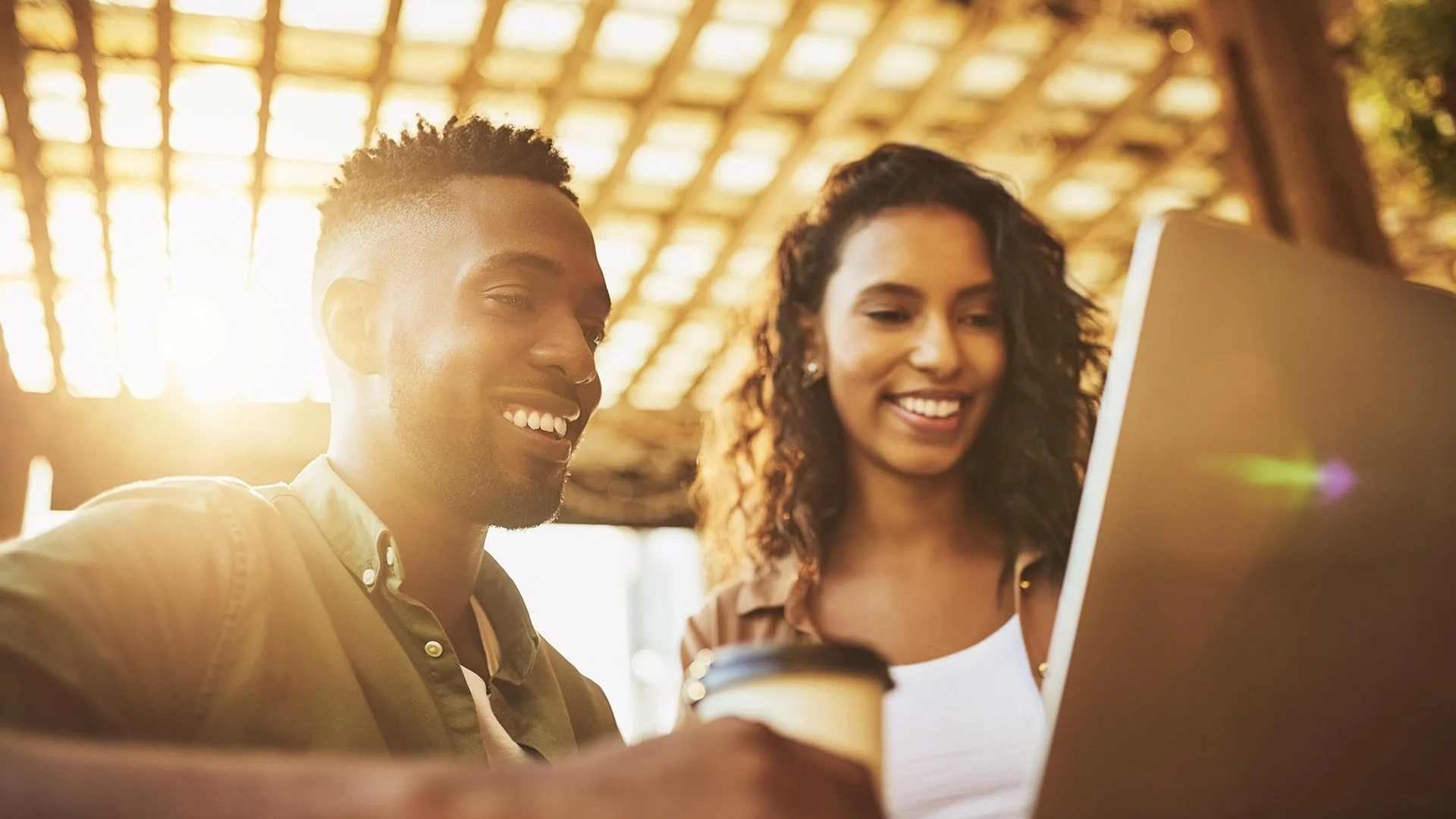 Homens e mulher sorrindo ao olharem uma tela de computador, de manhã, em um ambiente iluminado com luz quente.