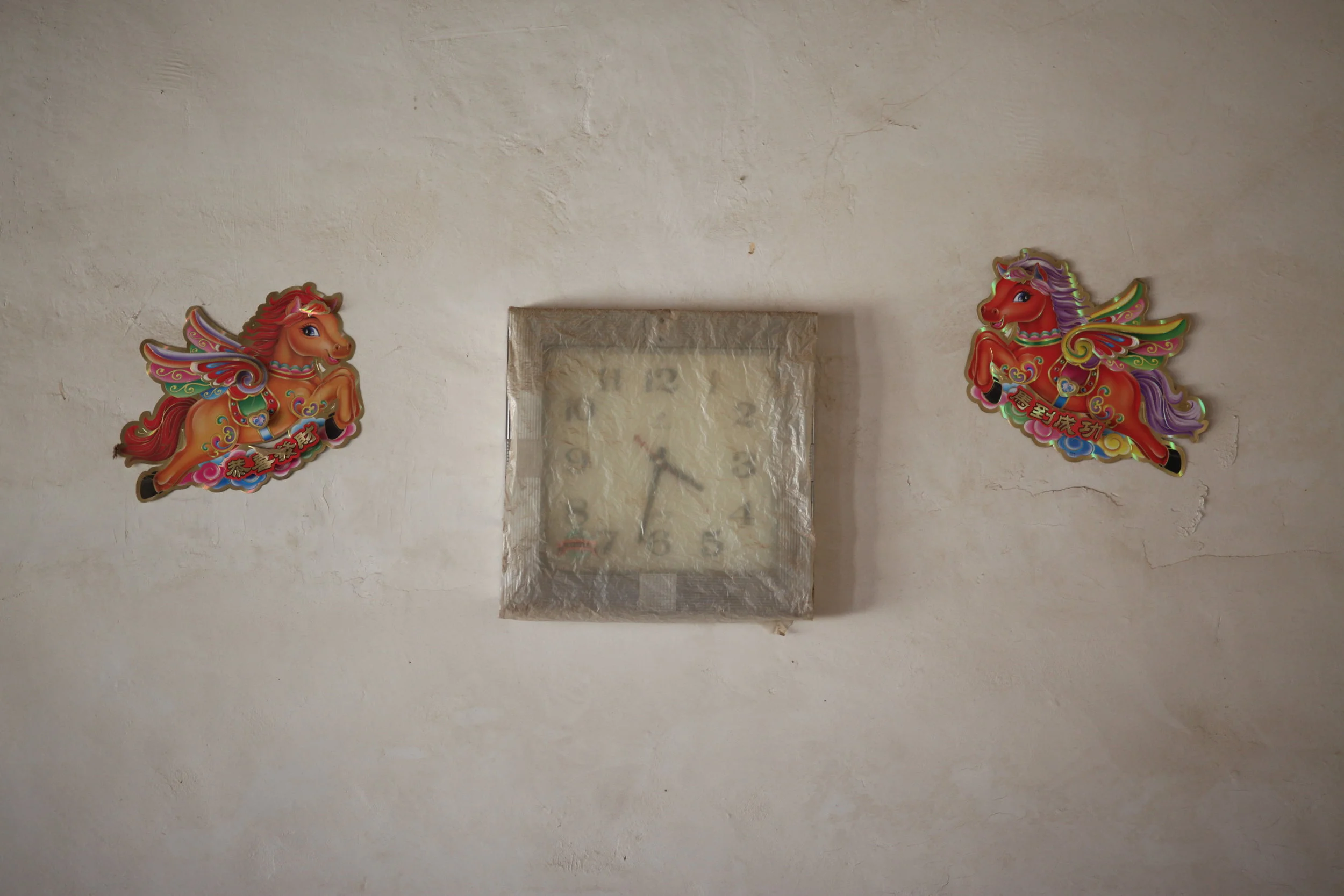 A clock with a wrapped, reflective surface, flanked by colorful cartoon-style horse decorations on a textured wall.
