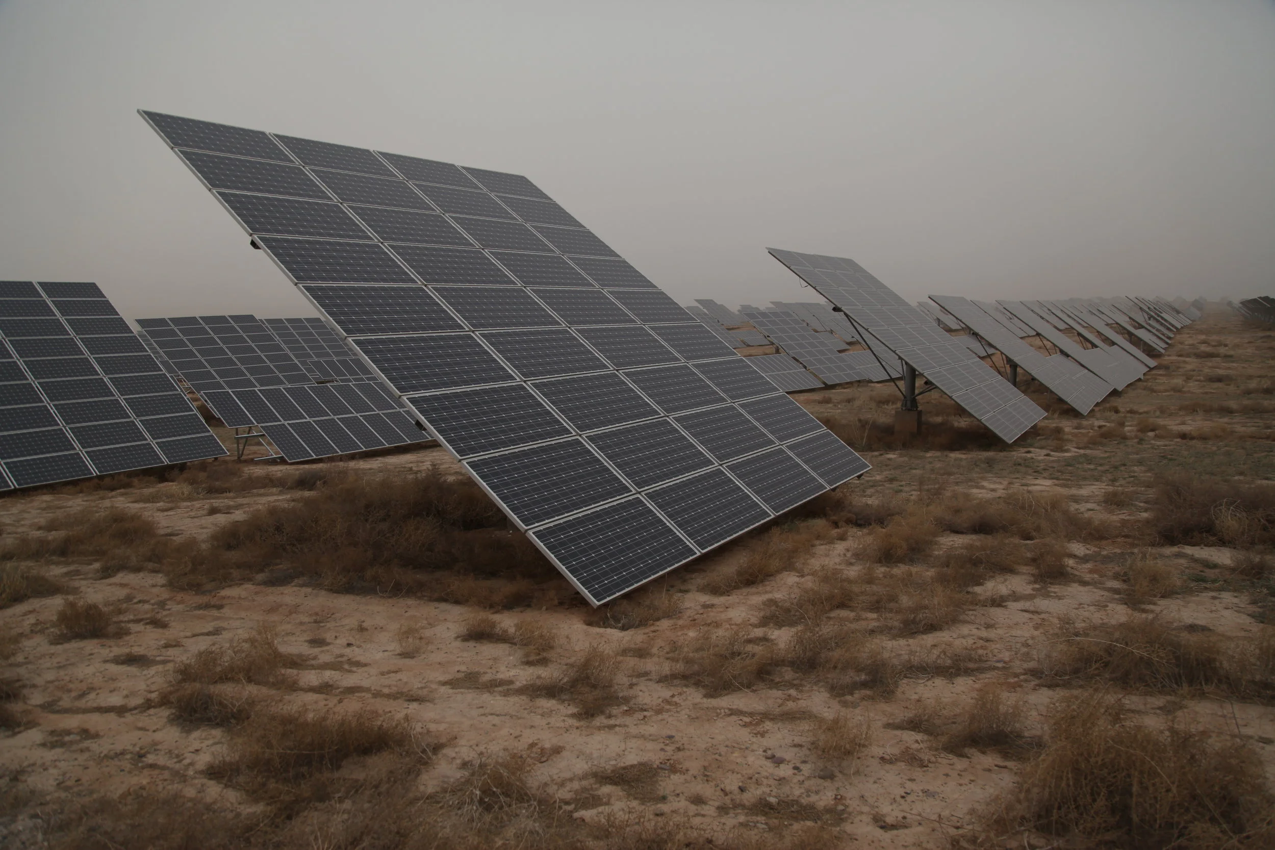 Multiple solar panels installed in a desert landscape under cloudy sky.