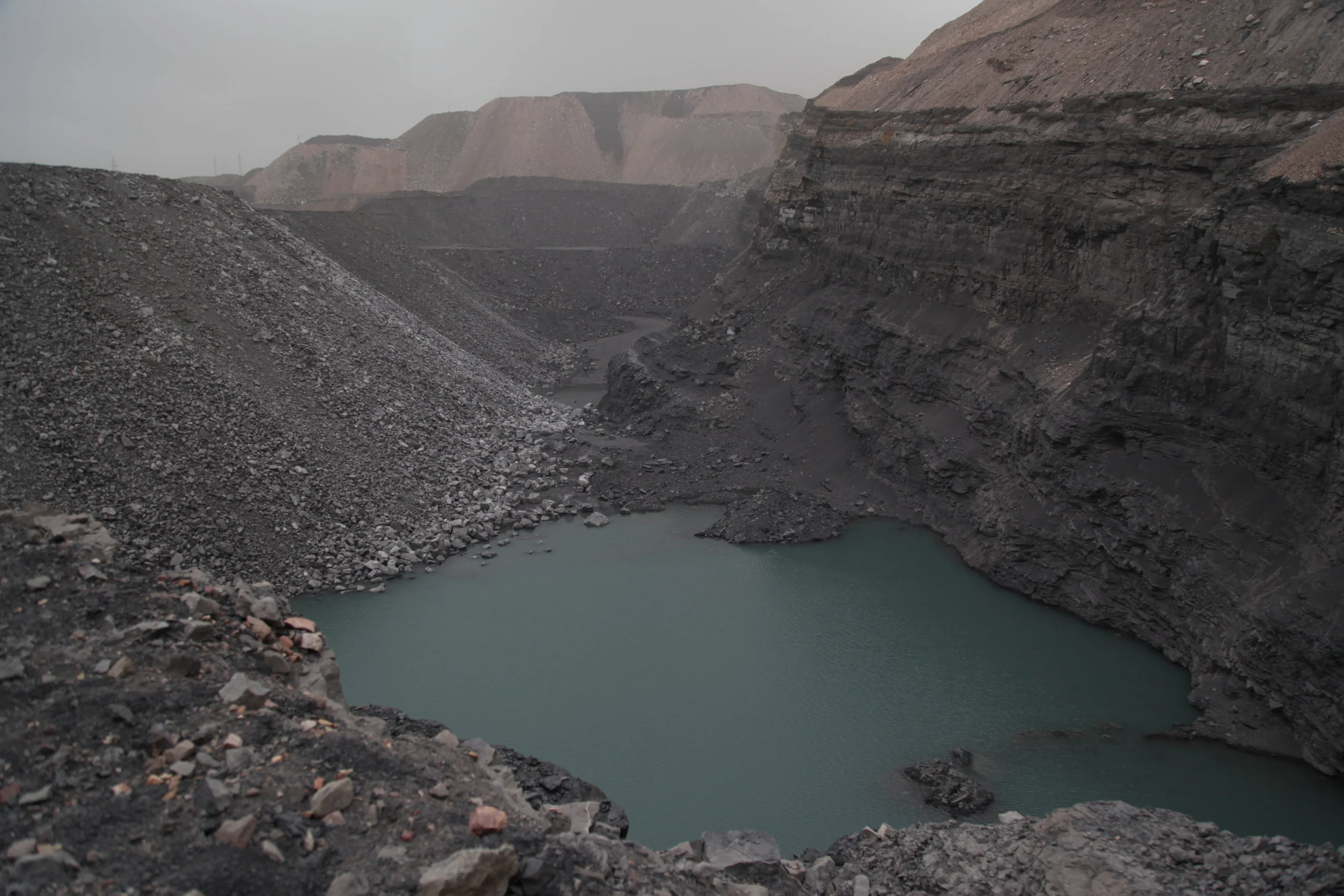 View of a large open-pit mining site with steep rocky walls and a small body of water at the bottom.