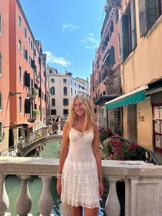 Woman in a white dress standing on a bridge over a canal in Venice, Italy.