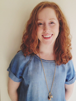 Smiling girl with curly red hair wearing a blue shirt and a necklace