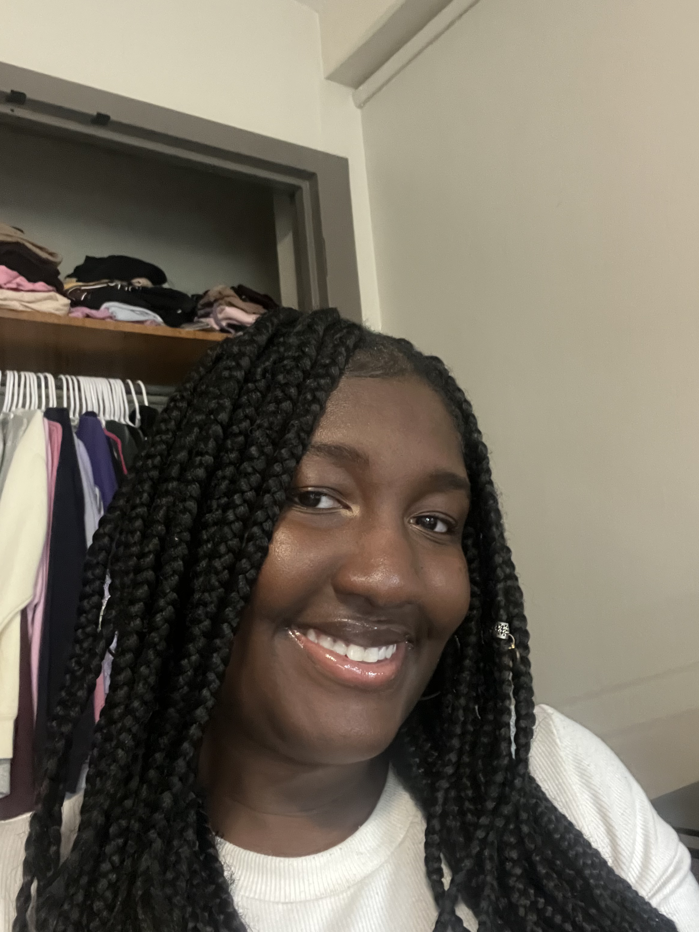 A woman with dark braided hair smiling indoors with an open closet in the background.