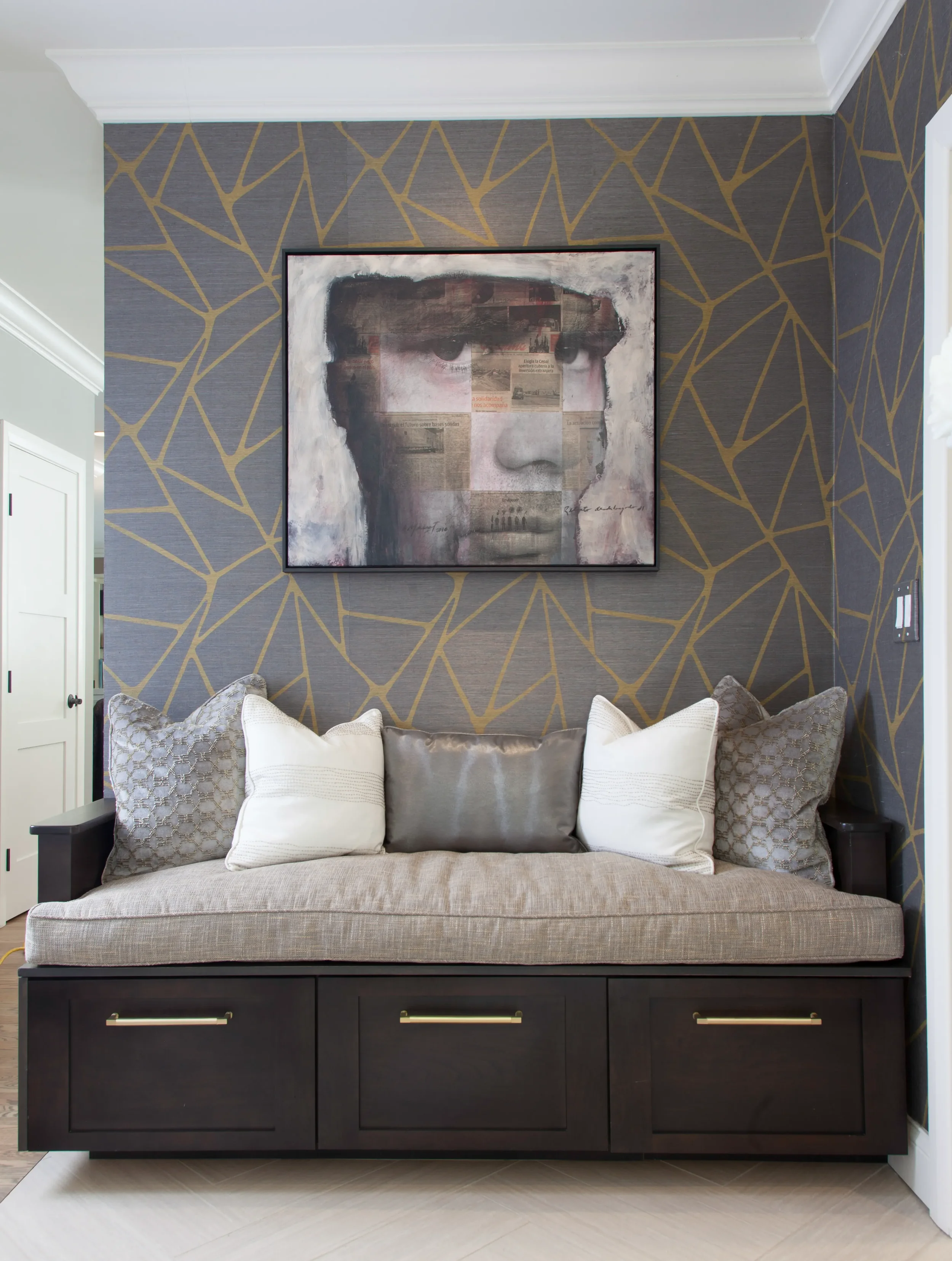 Custom storage bench with neutral cushions and pillows set against a gold and grey geometric wallpaper accent wall with framed artwork.