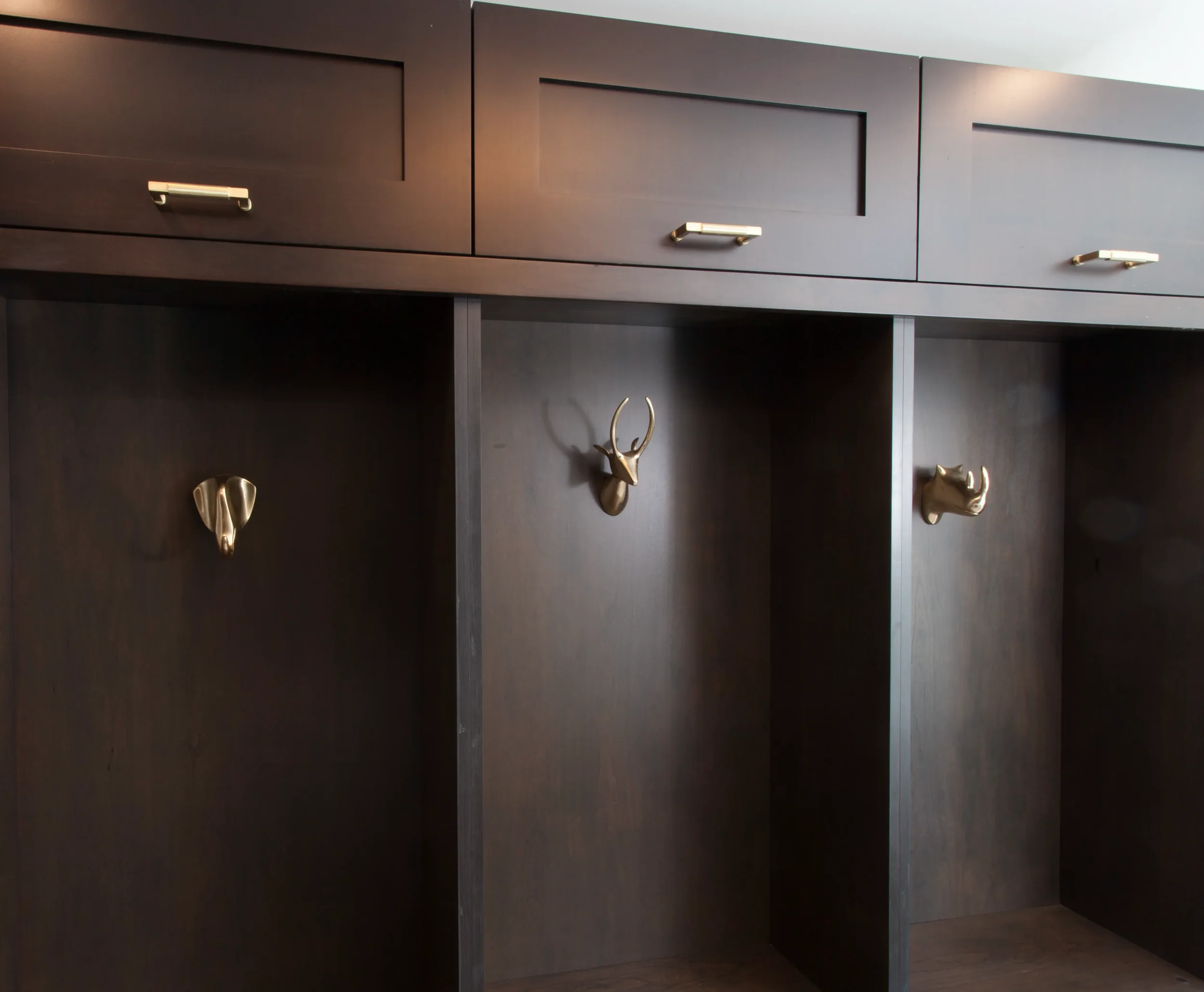 Close-up of a built-in storage nook with dark wood finishes, grasscloth texture, and a vintage-style brass animal hook.