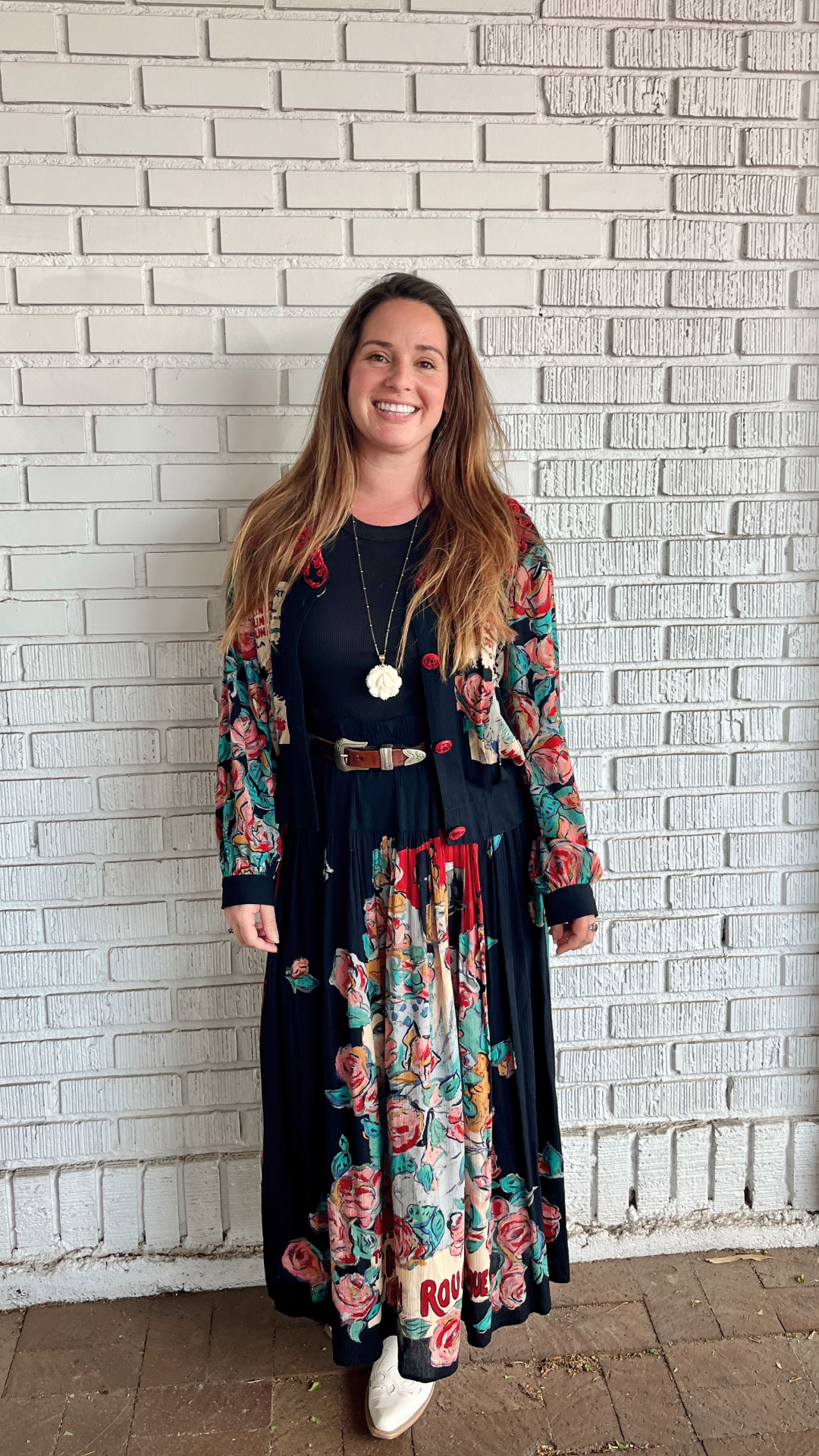 A woman wearing a vintage-inspired floral dress and matching cardigan against a simple brick backdrop.
