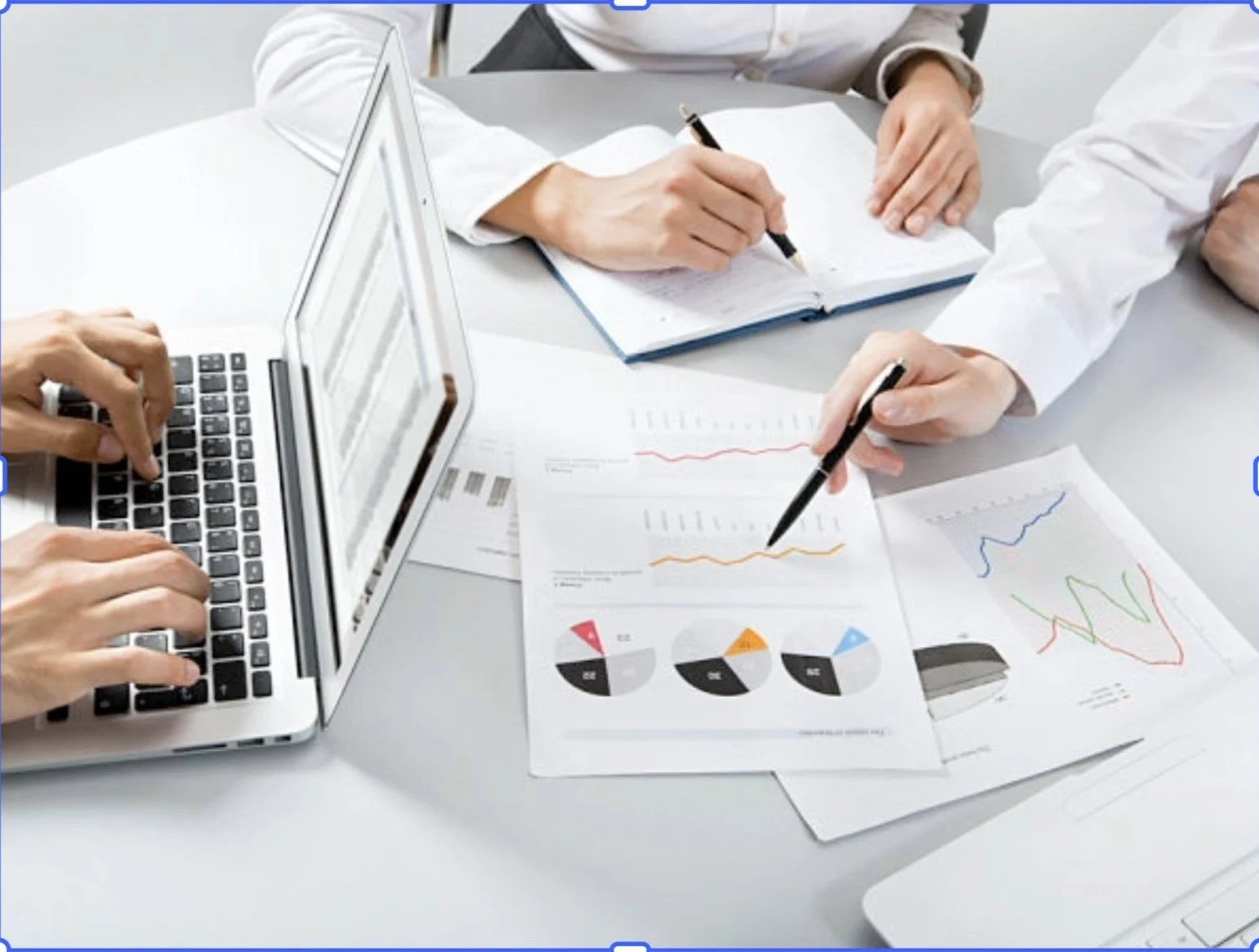 Personas trabajando en una mesa con gráficos, informes y una computadora portátil, analizando datos financieros.