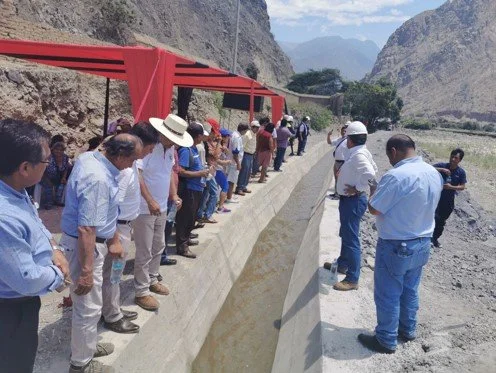 Grupo de personas observando una construcción de concreto en un paisaje montañoso