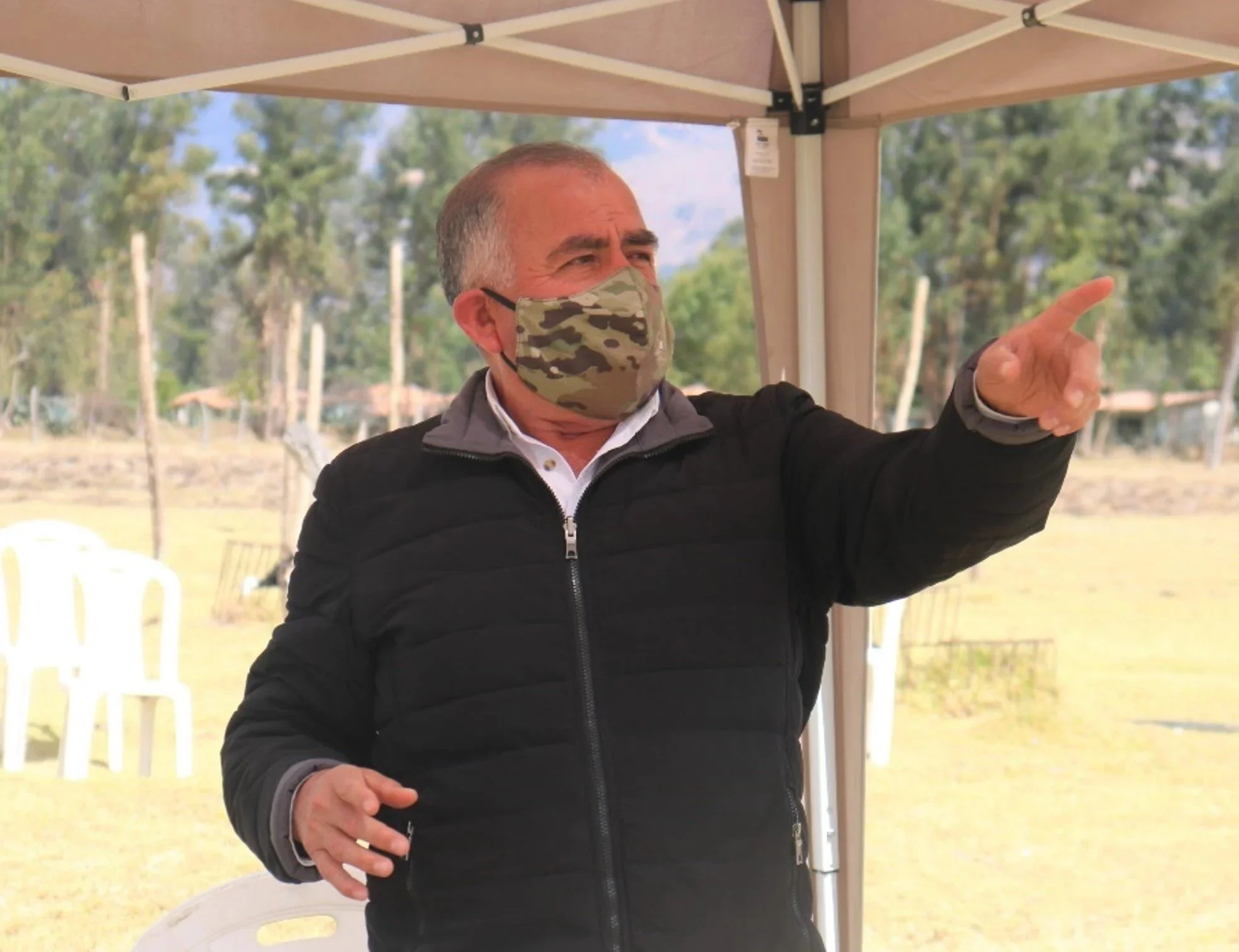 Hombre con mascarilla de camuflaje señalando hacia la derecha en un entorno al aire libre.