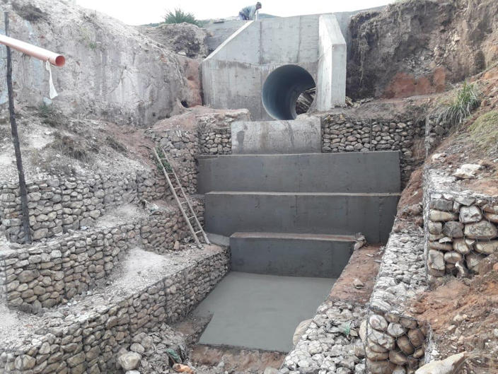 Escenario de construcción con una tubería grande y una estructura de concreto, en un terreno excavado.