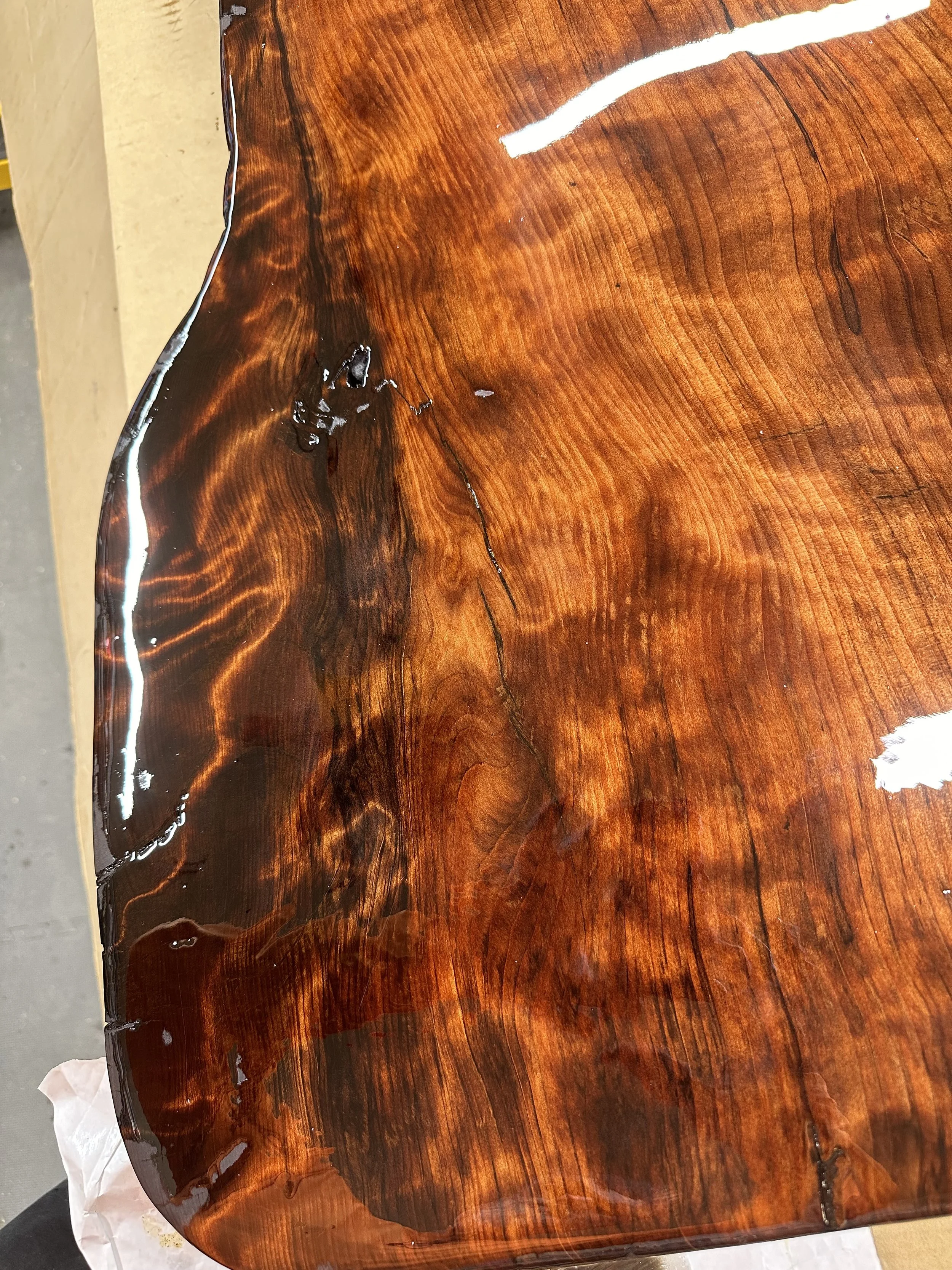 Close-up of a wooden surface with a rich, glossy finish showing natural wood grain patterns and some damage or irregularities on the surface.