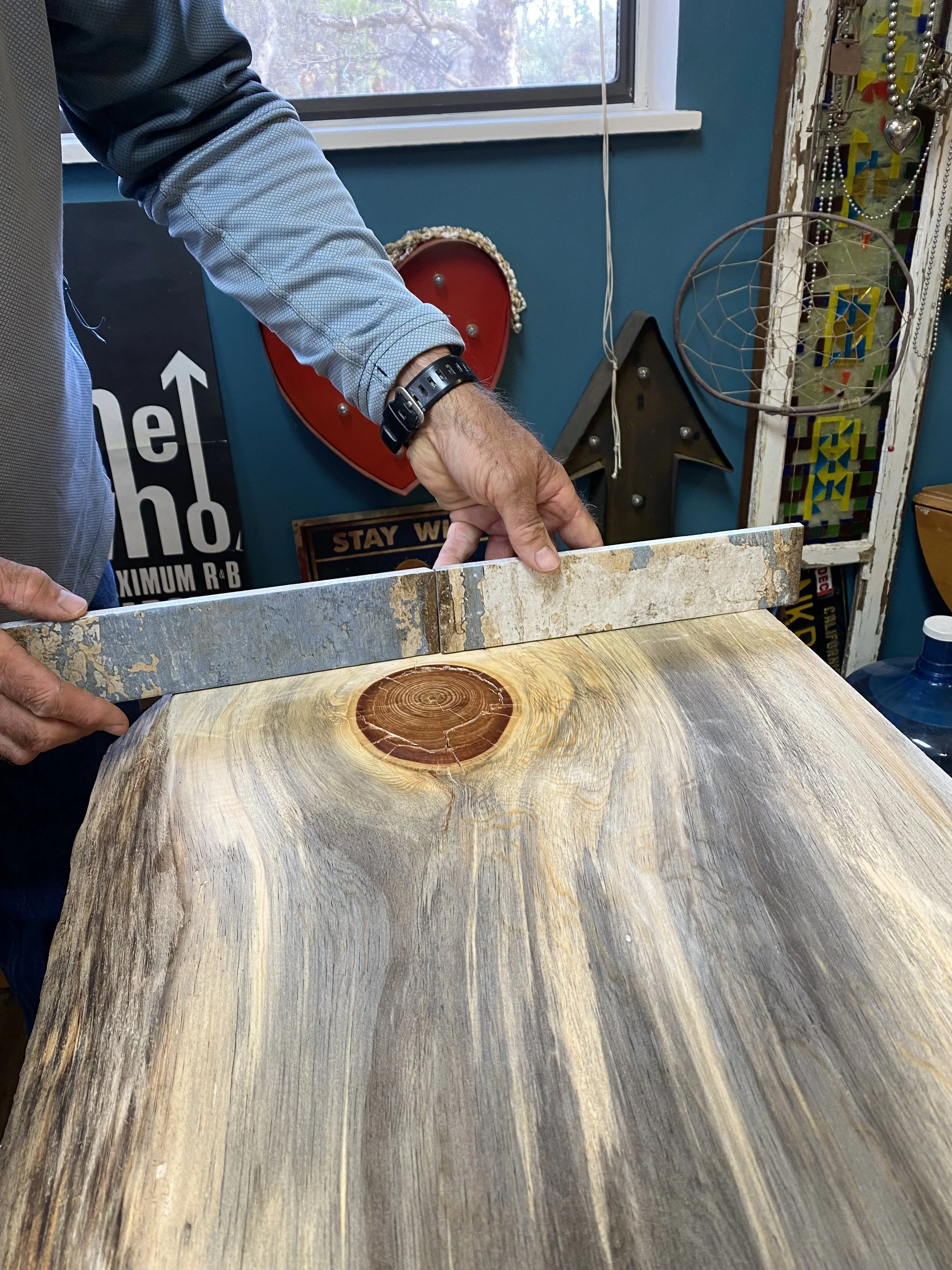 Person holds a straight piece of stone up to a beautiful wooden slab, highlighting the colors and clean cut quality of the slab