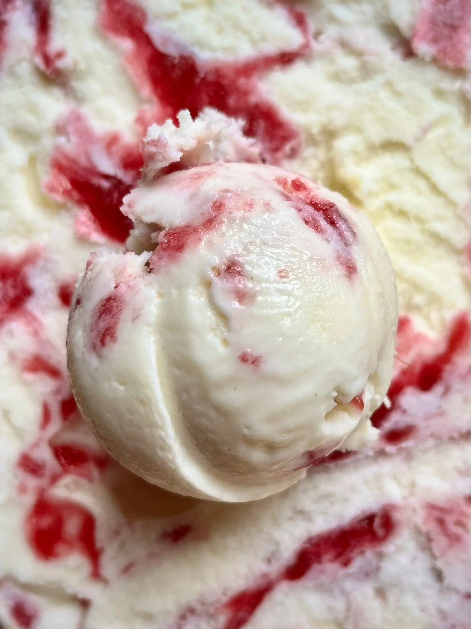 Een bolletje vanille-ijs met stukjes aardbei op een schep van aardbeienijs, omgeven door slagroom en stukjes aardbei.