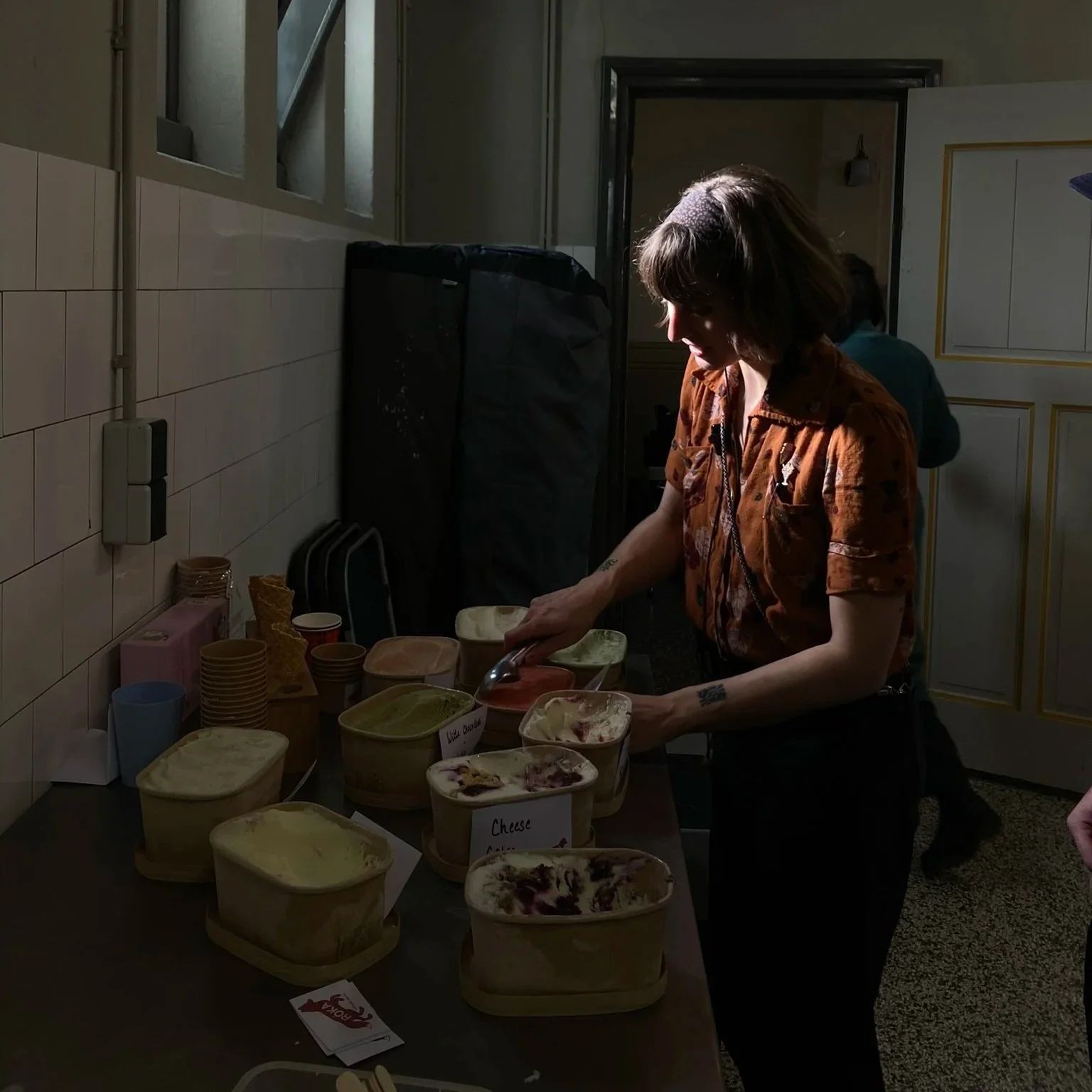 Vrouw die ijs schept op een tafel met verschillende ijsbakken in een keuken of cafe.