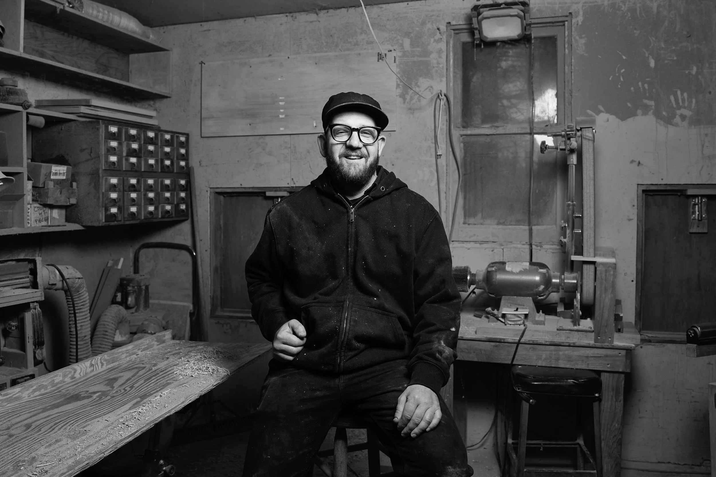 Portrait of a smiling Aaron Speiser seated on a stool in the workshop at Danby Hardwoods
