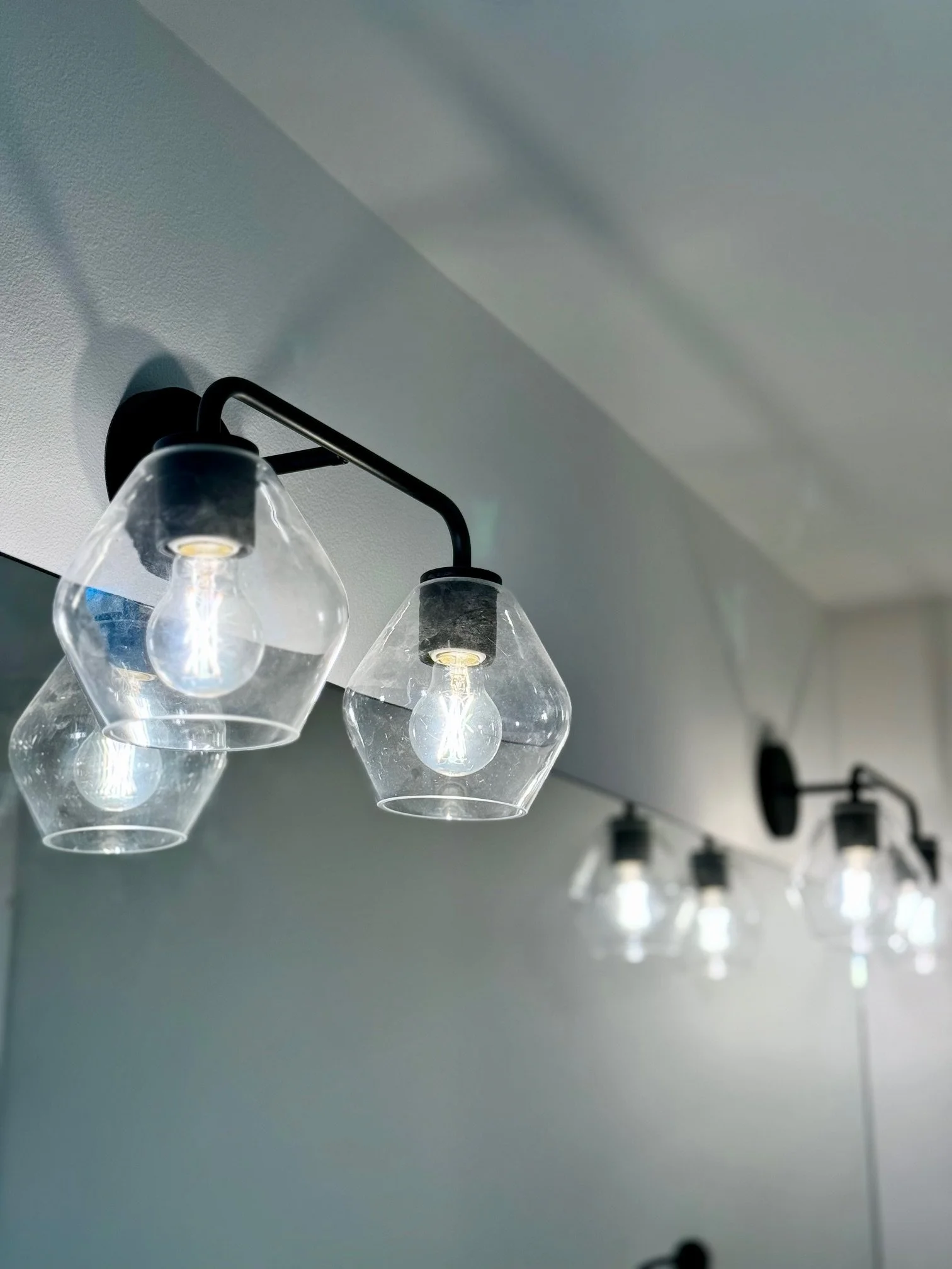 Close-up of a modern wall-mounted light fixture with clear glass shades around light bulbs, installed on a white wall.