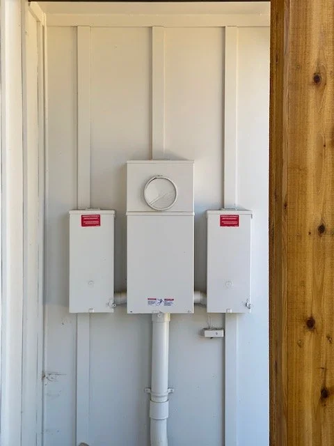 Electrical meter box with two fuse boxes on a wooden wall.