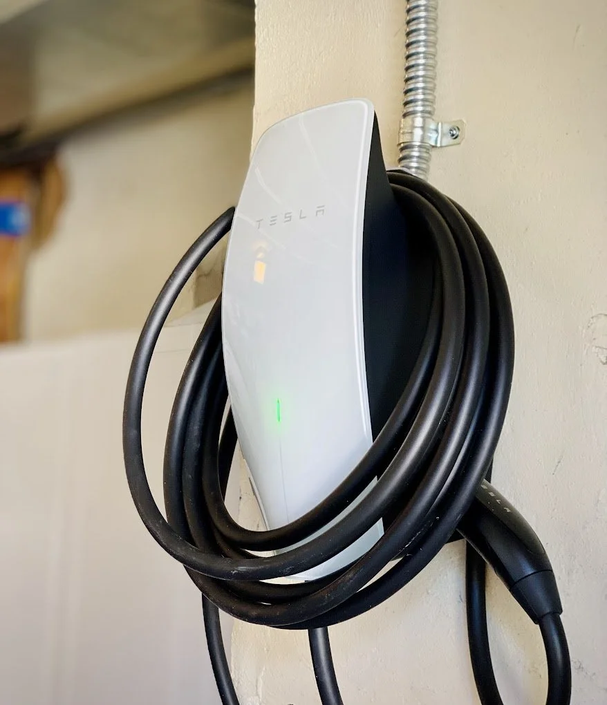 Tesla electric vehicle charger mounted on a beige wall with black charging cables coiled on it.