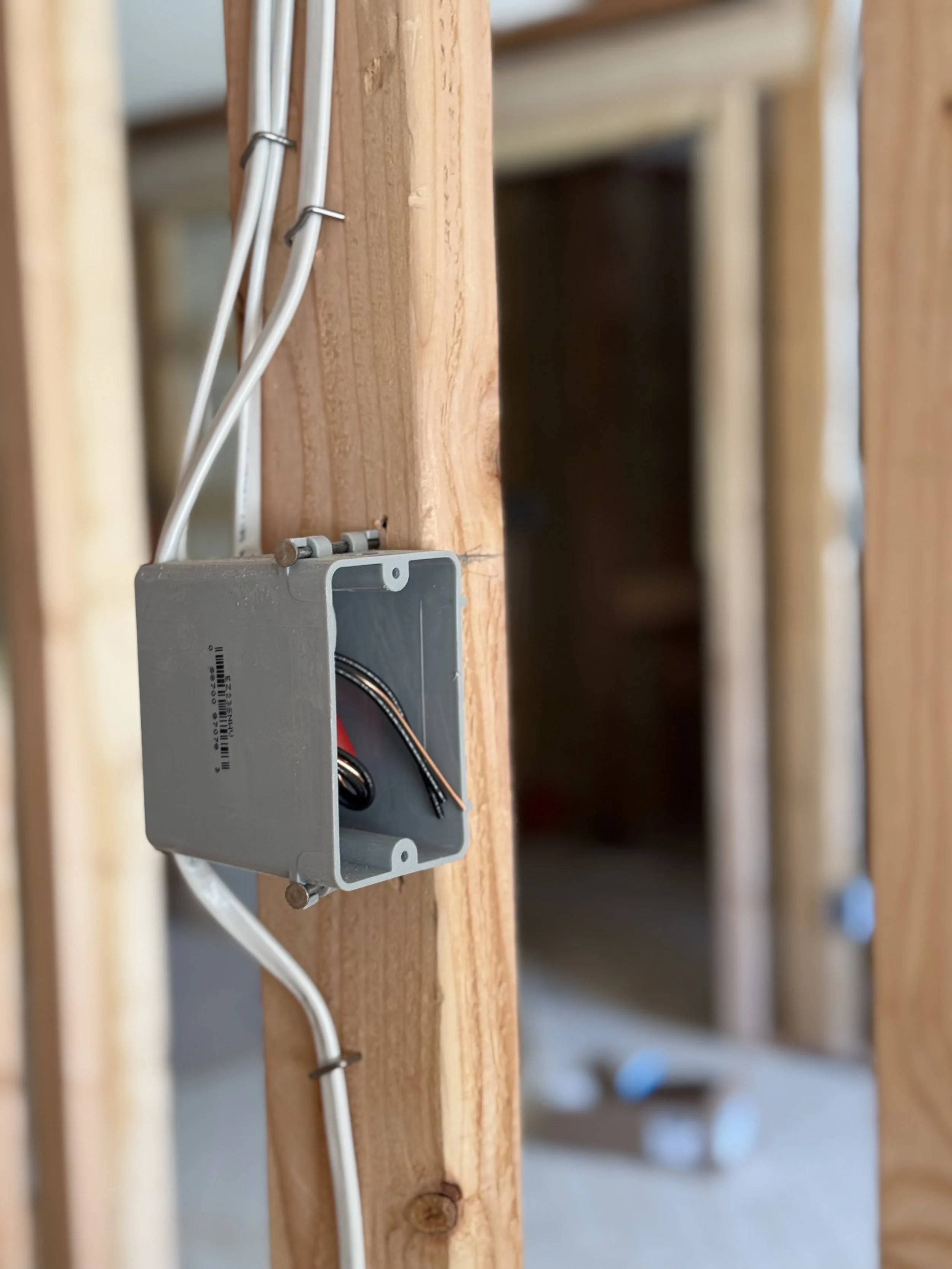 An electrical box mounted on a wooden wall with wires inside and some wiring attached to white cables.