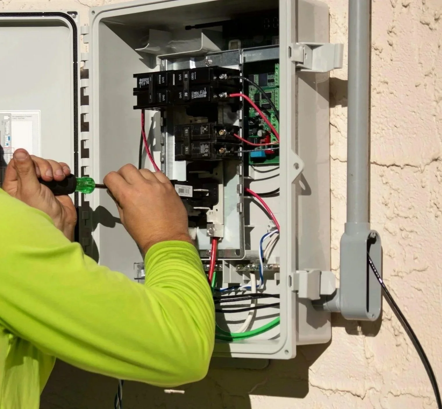 Technician wiring an electrical panel outside on a textured wall.