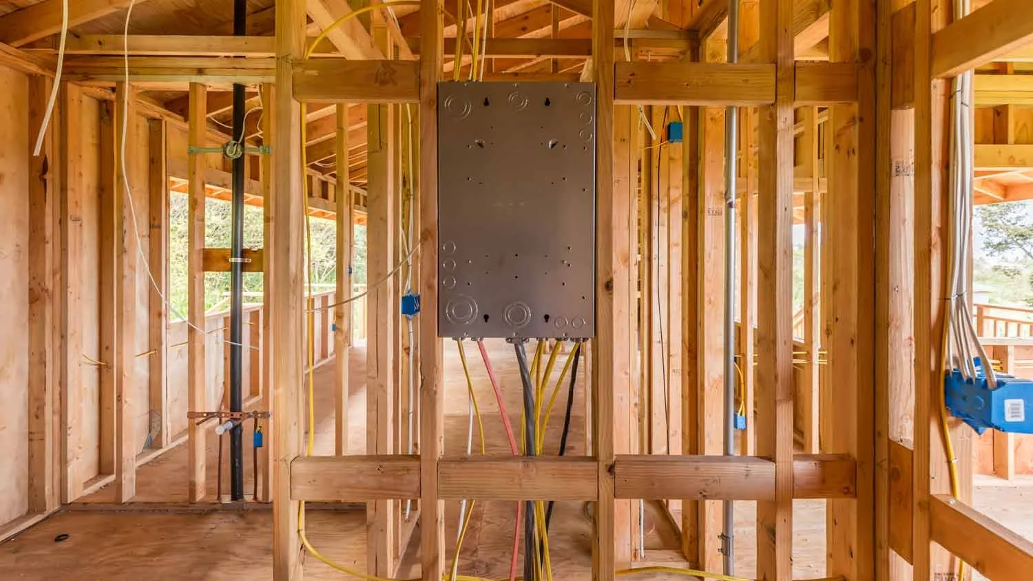 Construction site showing the wooden framing of a building with electrical wiring and a gray electrical panel mounted in the center.