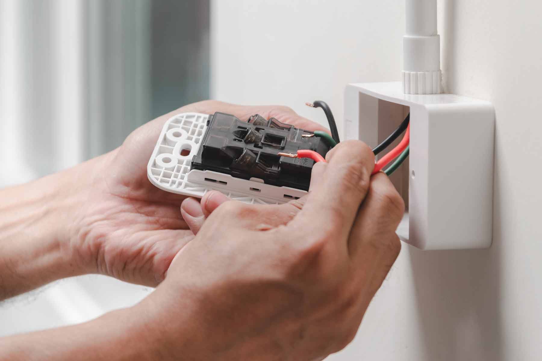 A person wiring an electrical device into an outlet on a wall.