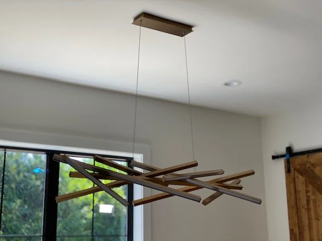 Modern wooden chandelier hanging from the ceiling with exposed bulbs, in a room with black window frame and wooden door.