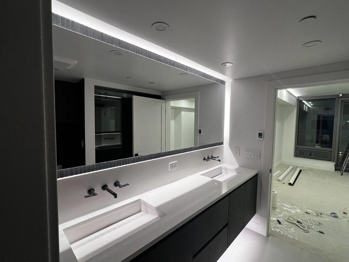 Modern bathroom with double sinks, large mirror, and under-cabinet lighting, appearing to be under construction or renovation.
