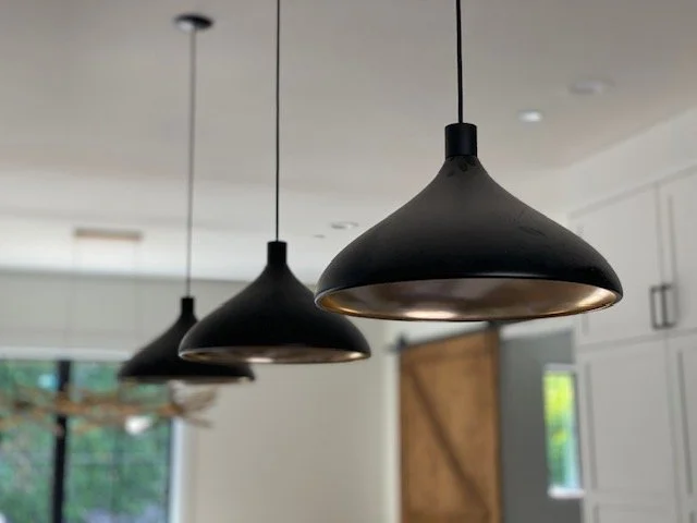 Three black pendant light fixtures hanging from the ceiling over a kitchen area.
