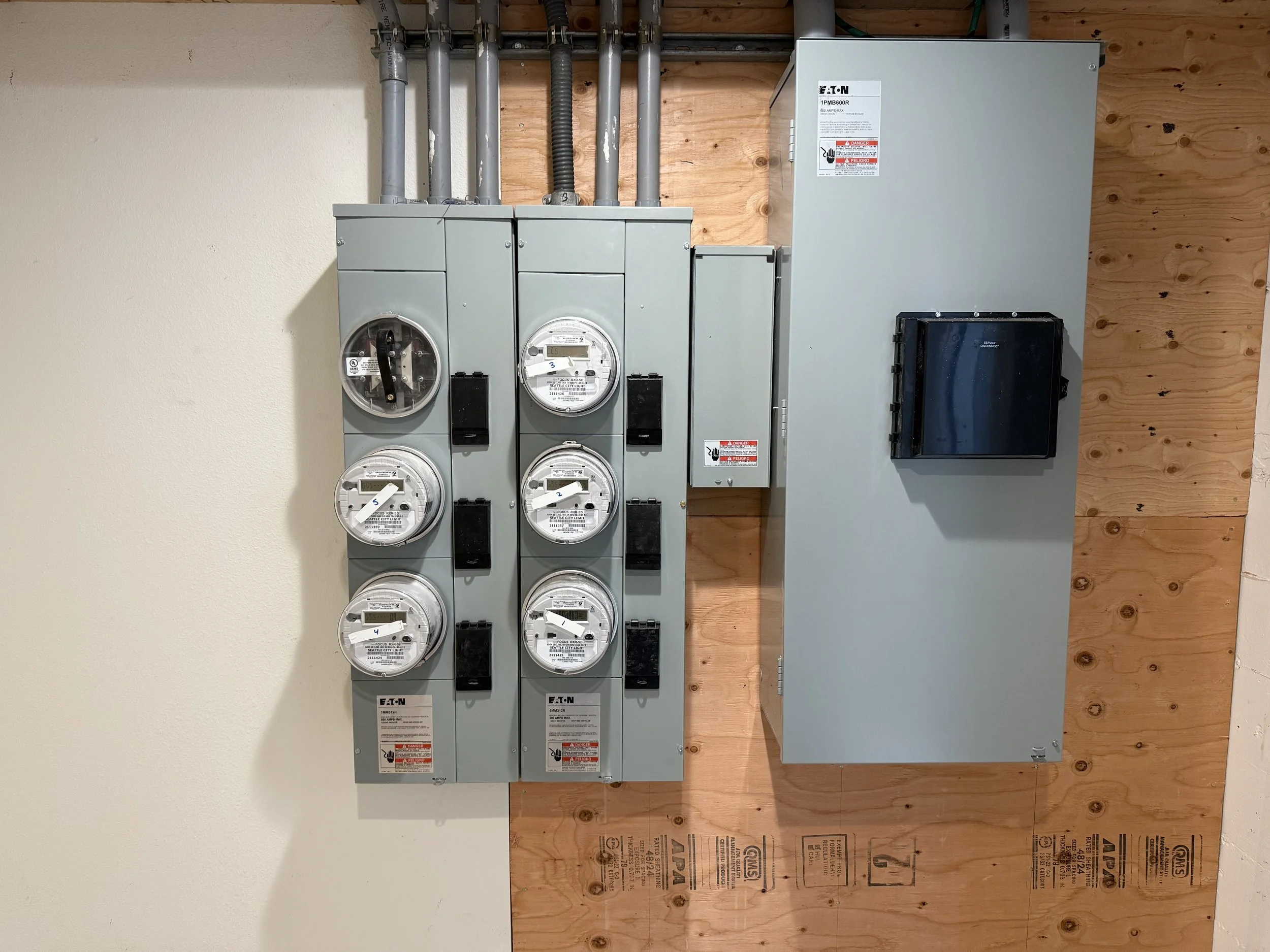 Electrical meters and electrical panel mounted on a wooden wall in a utility room.