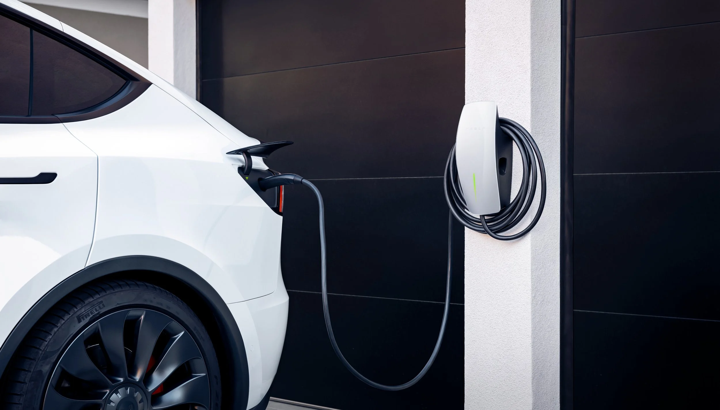 A white electric car is plugged into a wall charging station in a modern garage.