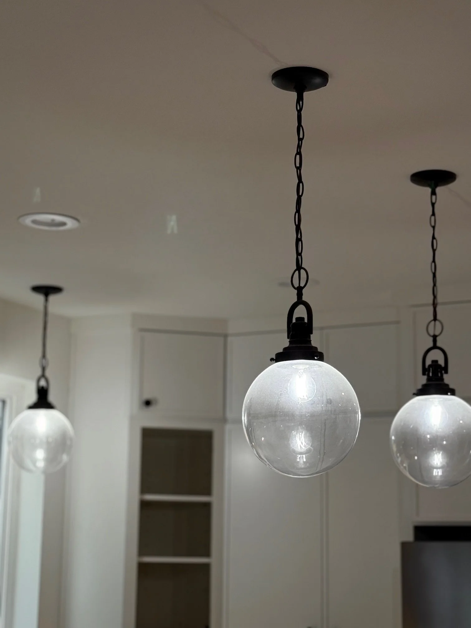 Three hanging pendant lights with glass globes in a modern kitchen.