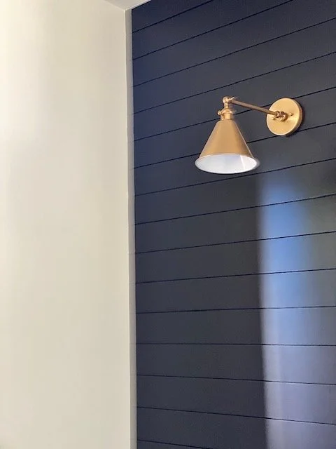 A brass wall-mounted lamp attached to a dark blue wooden paneled wall in a room.
