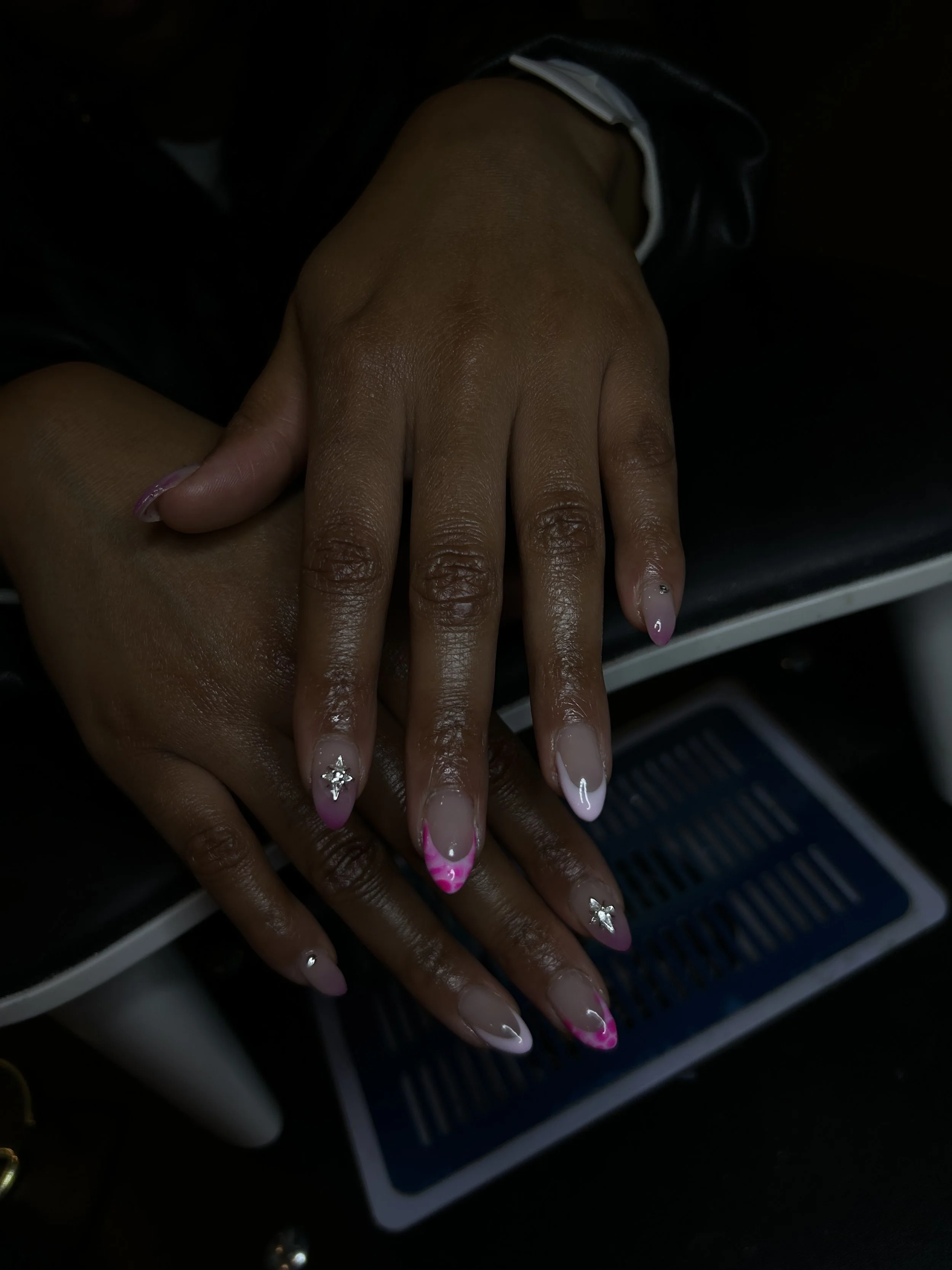 Close-up of hands with decorated french manicure nails, featuring pink tips and rhinestone embellishments.