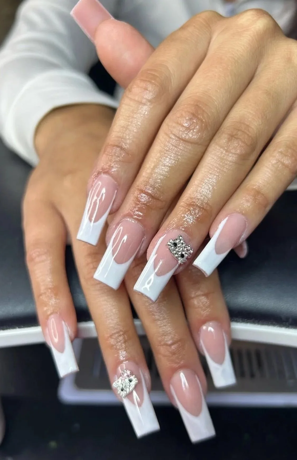 Nail art with white French tips and two rhinestone crown embellishments on the ring fingers of both hands, set against a dark background.