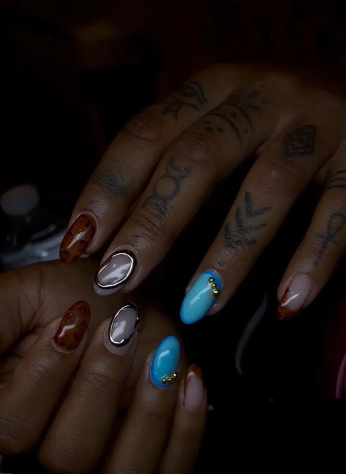 Close-up of hands with colorful nail polish and tattoos.