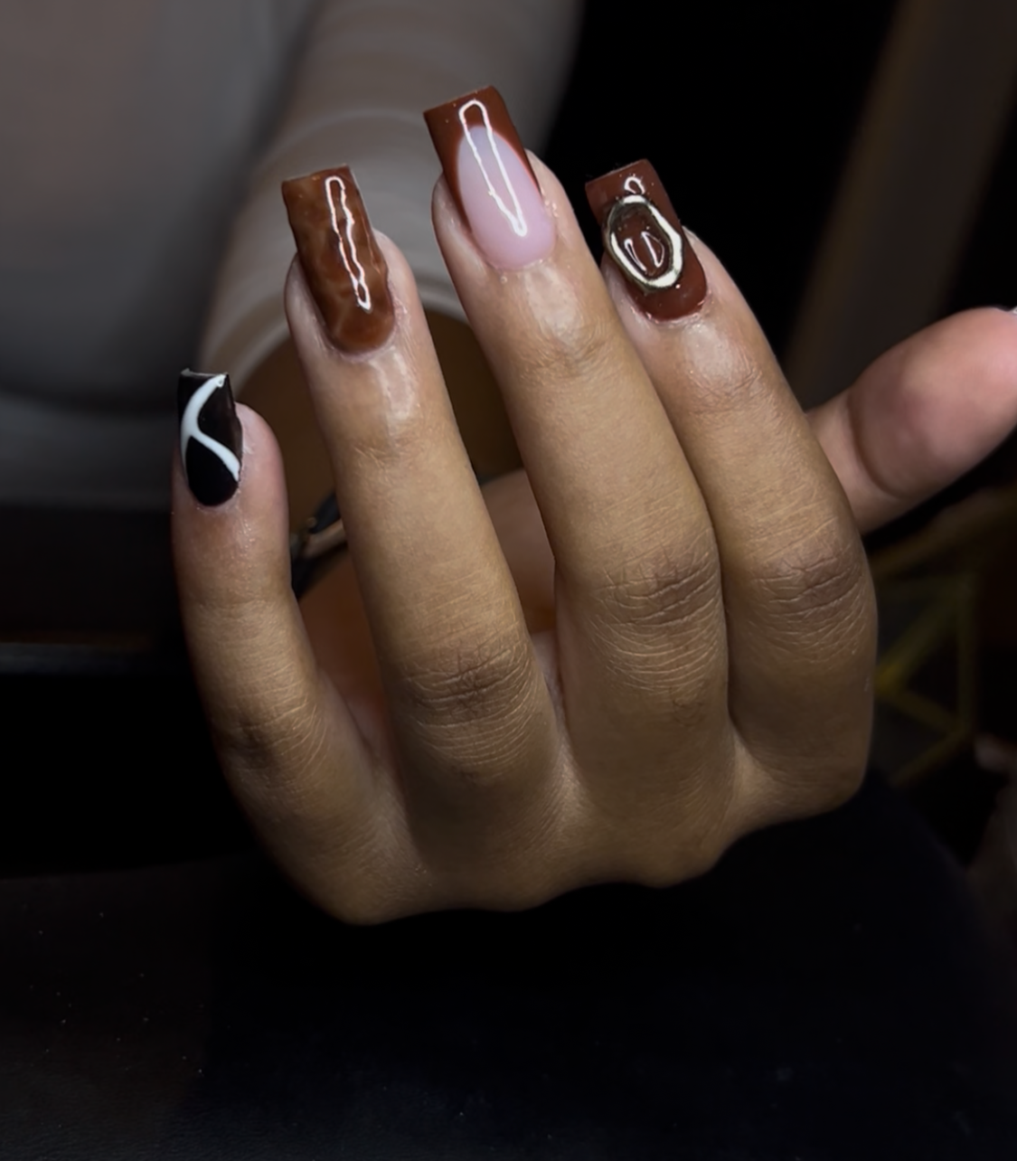 Close-up of a hand with manicured nails painted in different designs, including black, white, pink, and brown colors