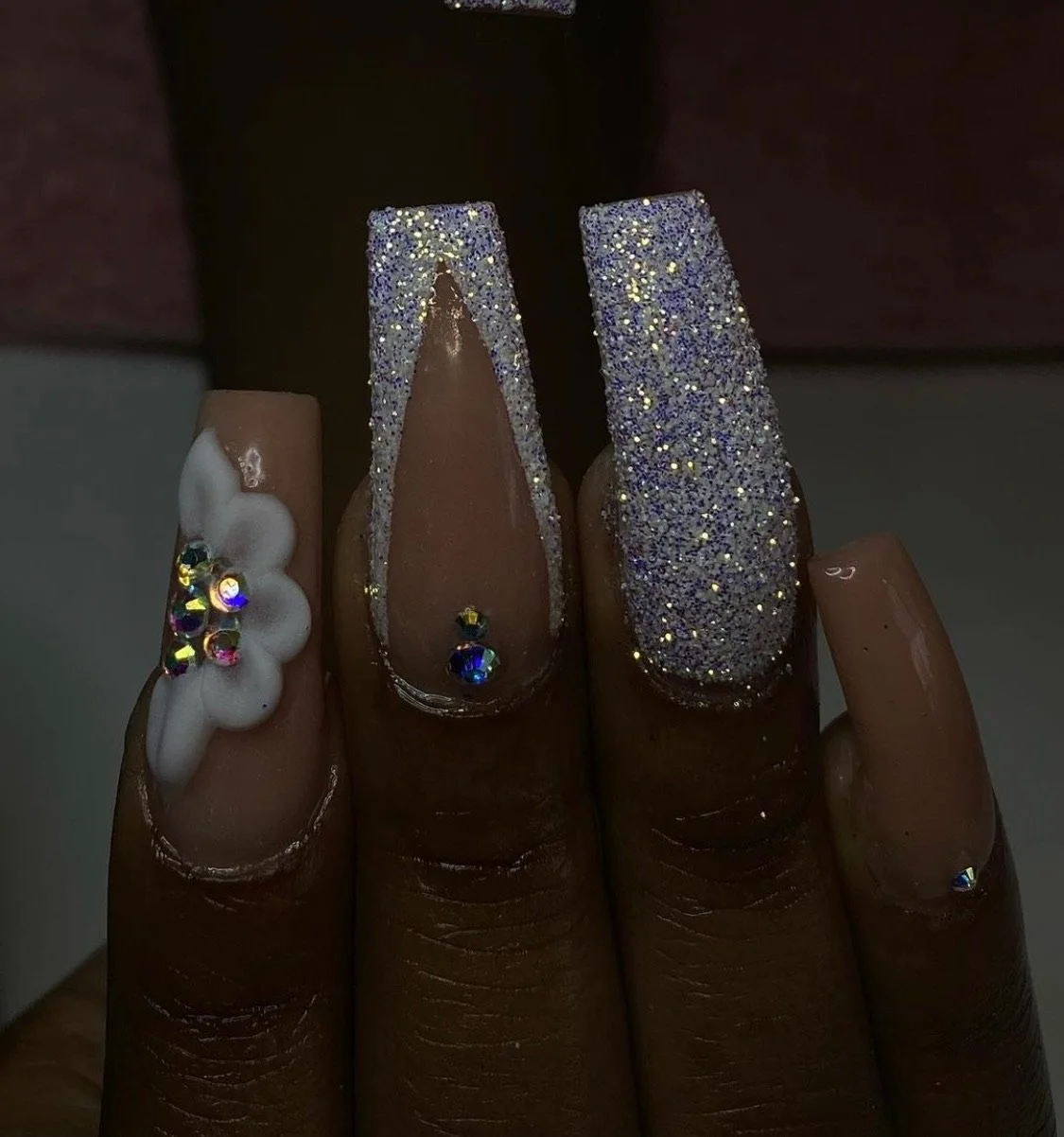Close-up of decorated fingernails with glitter, rhinestones, and floral design on one nail.