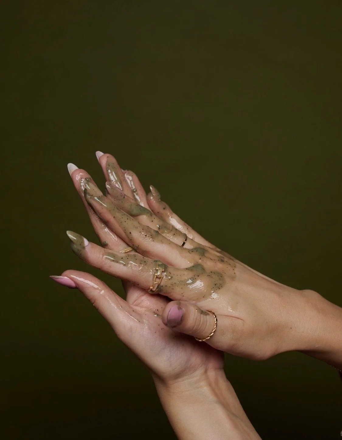 Hands covered in a brown, mud-like substance, with a dark green background.